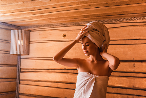 Young woman fixing towel on head in sauna