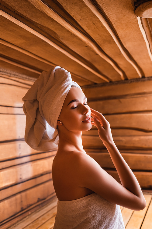 Young woman in white towels standing in sauna
