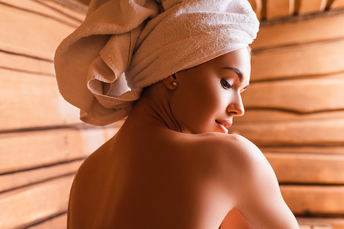 shirtless woman with towel on head relaxing in sauna
