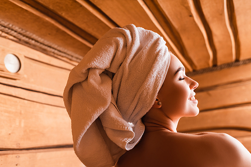 smiling woman with towel on head and naked shoulders resting in sauna