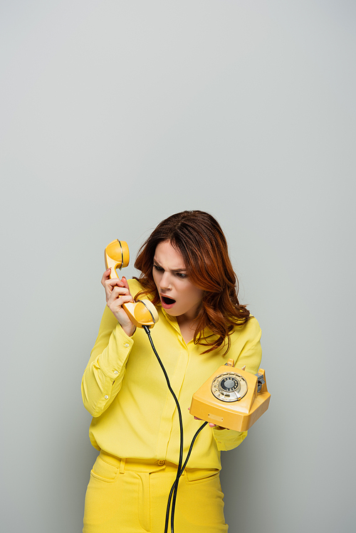 angry woman screaming while holding vintage phone on grey