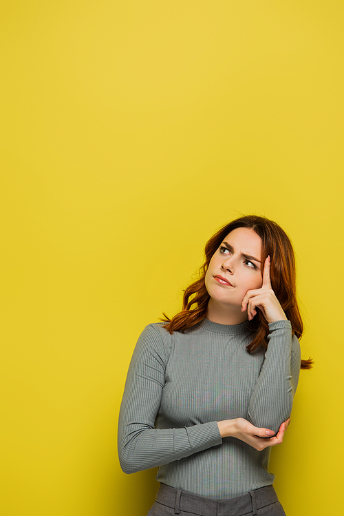 worried woman touching head and looking away while thinking on yellow