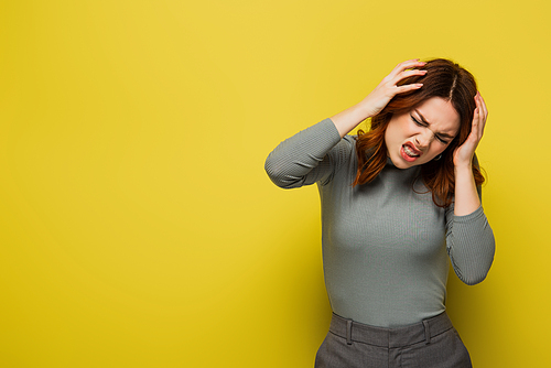 stressed woman touching head while suffering from migraine on yellow