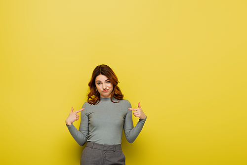 displeased woman with curly hair pointing with fingers at herself on yellow