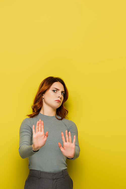 displeased woman with wavy hair showing stop gesture and  on yellow