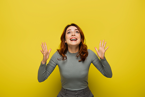 amazed woman with wavy hair gesturing while looking up on yellow