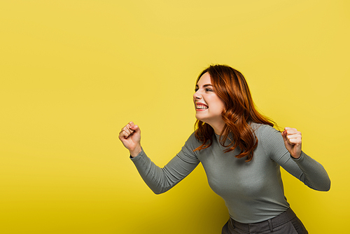 amazed woman with wavy hair and clenched fists on yellow