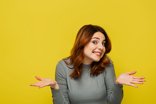 smiling woman with wavy hair showing shrug gesture isolated on yellow