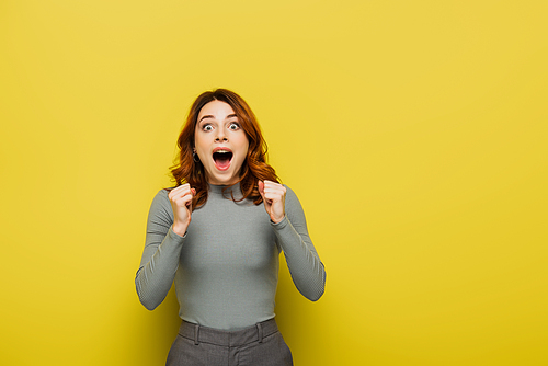 excited young woman with clenched fists  on yellow