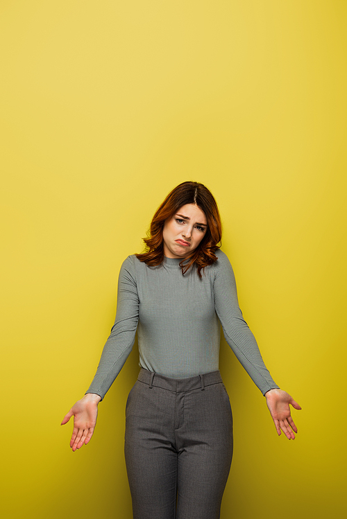confused woman with wavy hair showing shrug gesture on yellow