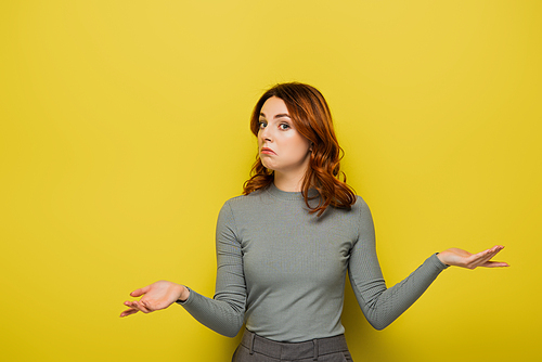 confused woman with wavy hair showing shrug gesture isolated on yellow