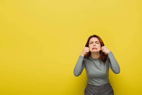 frustrated woman with clenched fists crying isolated on yellow