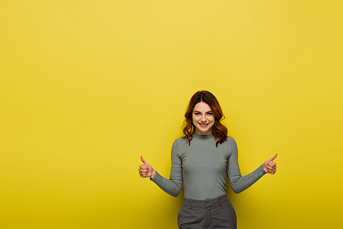 happy woman with curly hair showing thumbs up on yellow