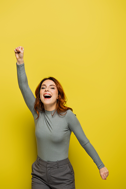 positive woman with curly hair and raised hand on yellow