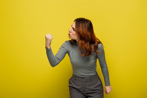 angry woman with curly hair showing clenched fist on yellow