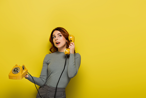 young woman sticking out tongue while holding retro telephone on yellow