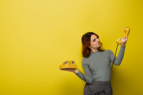displeased young woman looking at retro phone on yellow