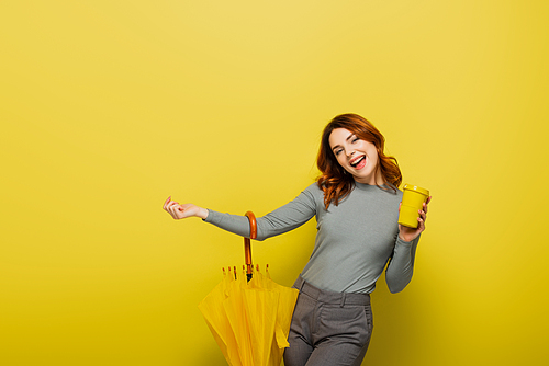 amazed woman with curly hair holding paper cup and umbrella on yellow