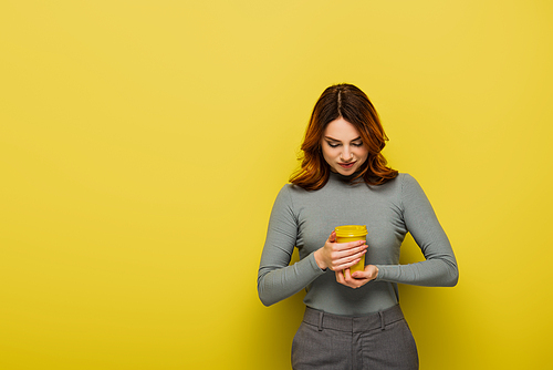 young woman with curly hair holding paper cup on yellow