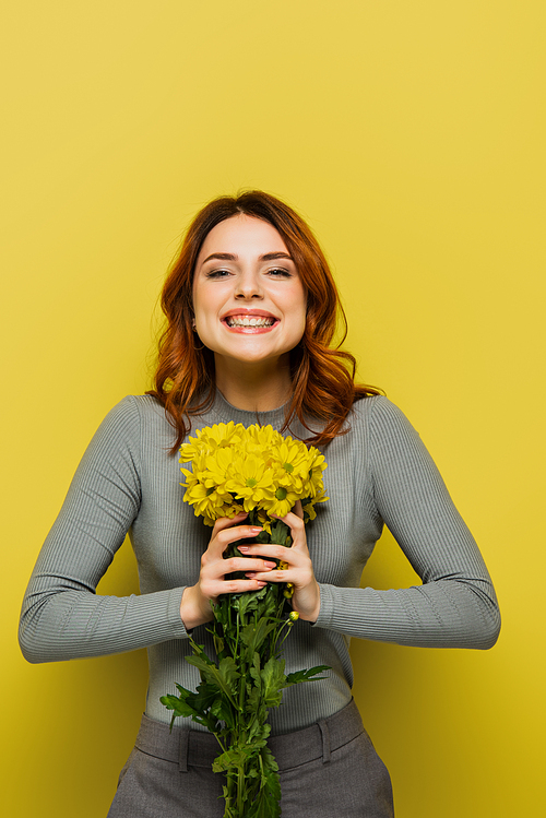 joyful young woman with wavy hair holding flowers on yellow