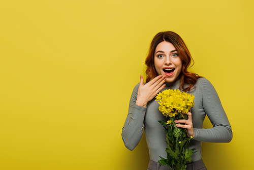 amazed woman with wavy hair holding flowers on yellow