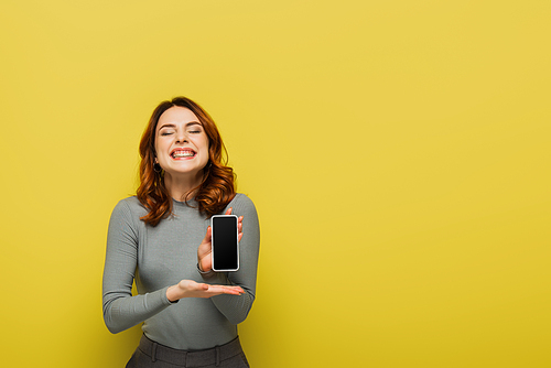 cheerful woman with closed eyes holding smartphone with blank screen on yellow