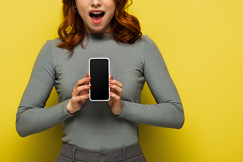 cropped view of surprised woman holding smartphone with blank screen on yellow