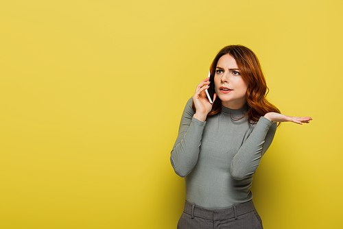 young displeased woman with curly hair talking on smartphone on yellow