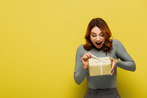 amazed young woman pulling ribbon on present on yellow