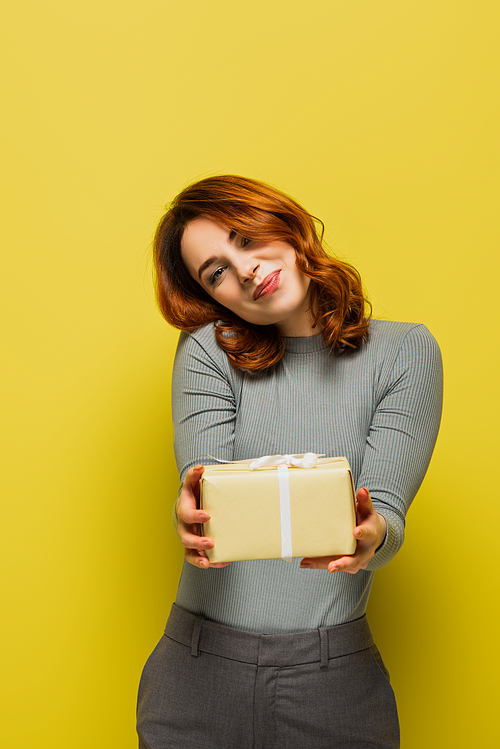 happy young woman holding gift box and smiling on yellow
