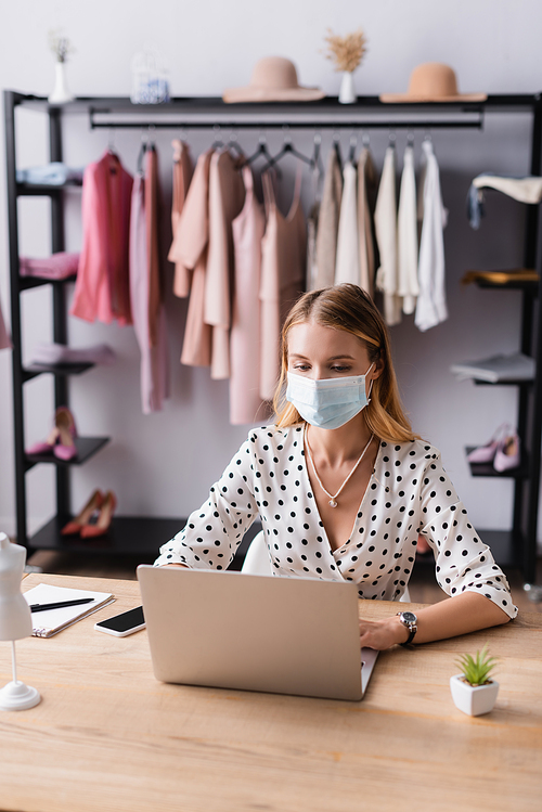 businesswoman in medical mask, working on laptop at workplace in showroom