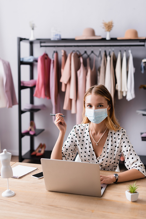 businesswoman in medical mask,  while sitting near laptop in showroom