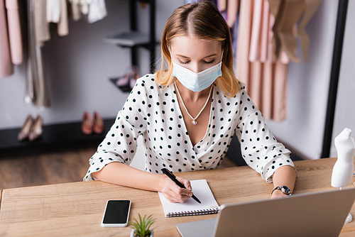 seller in medical mask writing order in notebook while working in showroom