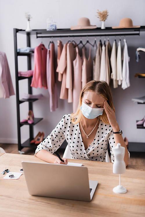 tired showroom owner in medical mask, suffering from migraine at workplace