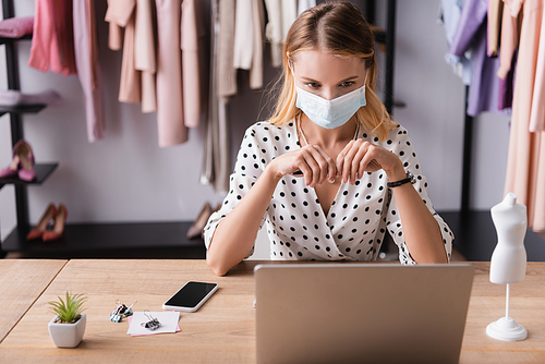 showroom owner working near laptop and smartphone in medical mask