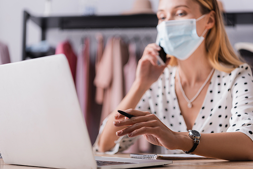 businesswoman in medical mask accepting order in showroom while working near laptop on blurred background
