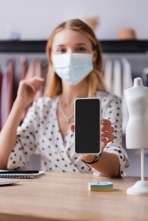 showroom owner in medical mask, showing smartphone with blank screen on blurred background