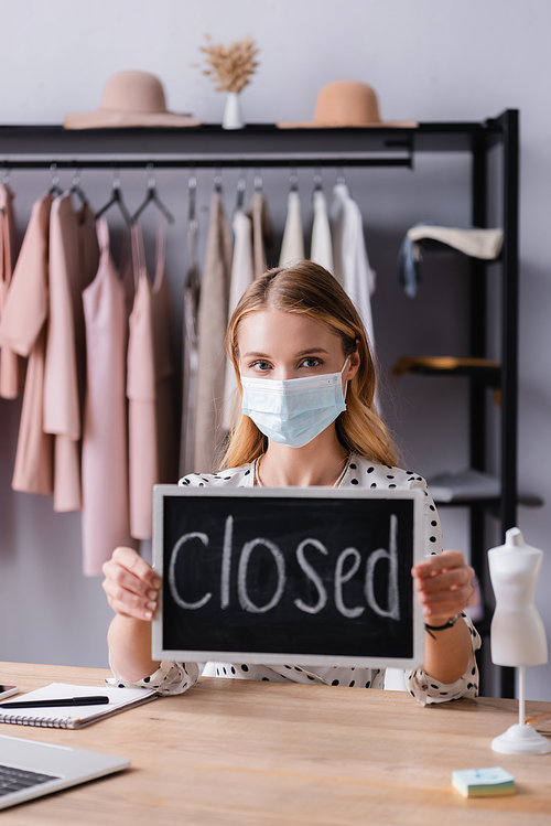 showroom owner sitting at workplace in medical mask and holding board with closed lettering