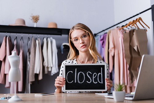 upset businesswoman holding board with closed lettering in showroom, blurred foreground