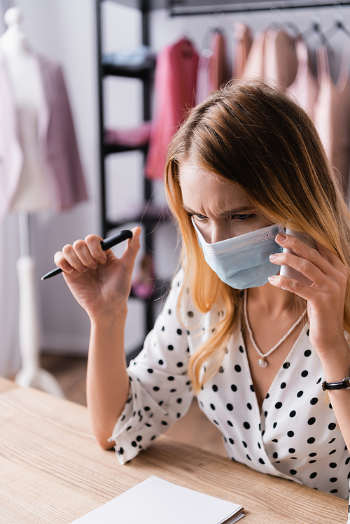 serious showroom owner accepting order on mobile phone while working in medical mask