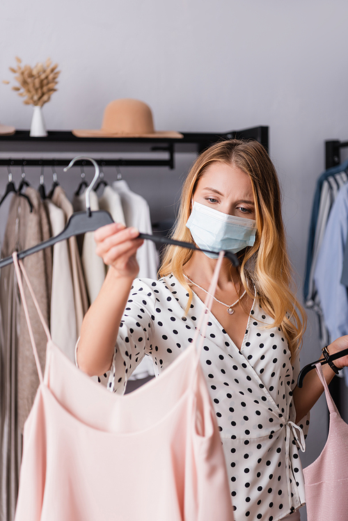 showroom owner in medical mask, holding hanger with dress on blurred foreground