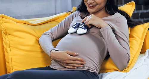 Cropped view of smiling pregnant woman holding baby booties