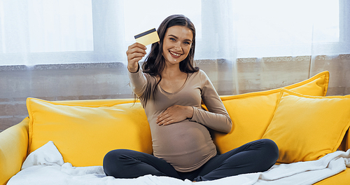 Smiling pregnant woman showing credit card in living room