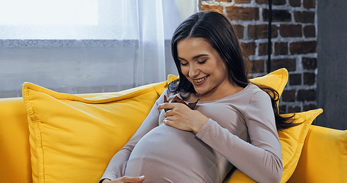 Cheerful pregnant woman holding cupcake at home