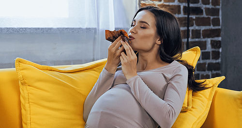 Pregnant woman eating cupcake in living room
