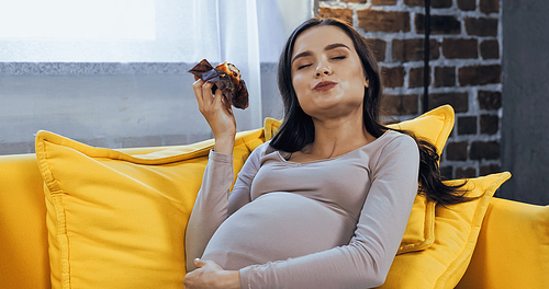 Pleased pregnant woman eating tasty cupcake