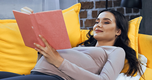 Pregnant woman reading book on blurred foreground at home