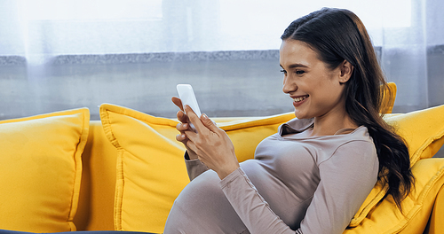 Pregnant woman with smartphone smiling while lying on couch