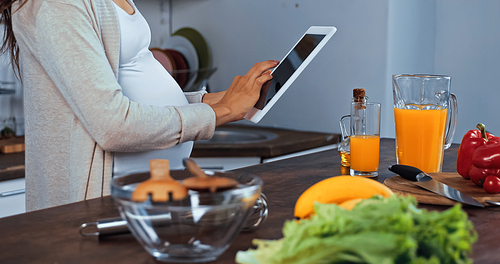 Cropped view of pregnant woman using digital tablet near food, oil and orange juice