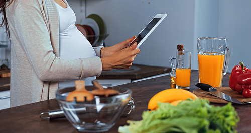 Cropped view of pregnant woman holding digital tablet near fresh food